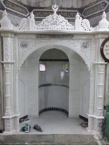 Supplier reference photograph of the white marble mosque qibla with carved columns, a broad arch, inscription panels and an ornamental crown