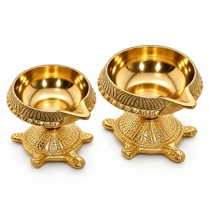 Set of two brass Kuber diyas with carved turtle bases on white background